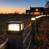 Square LED post cap light glowing on a fence post with a lit fence line receding at dusk
