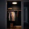 Motion sensor ceiling light switched on in a dark walk-in closet, lighting hanging shirts below