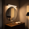Rotatable LED vanity light bar in silver lit at warm 3000K above a bedroom dressing mirror