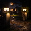 Two modern steel pillar lights on driveway gate posts lit warm in the rain at night