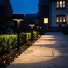 Three black bollard path lights in a row along a paved garden walkway at blue hour