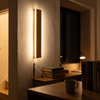 Rotatable wood side-glow wall lamp throwing a band of light in a study at night