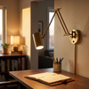 Compact gold swing arm wall sconce over a writing desk at golden hour