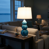 Lake blue gourd table lamp lit on a console behind a sofa at dusk