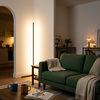 Slim corner floor lamp glowing warm white beside a green sofa