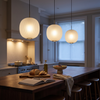 Three matte white globe pendant lights in a row over a walnut kitchen island
