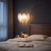 Black glass feather wall sconce glowing above a bedroom nightstand