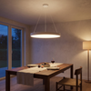 White round LED drum pendant light dimmed warm over a walnut dining table
