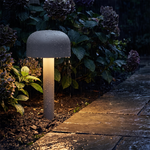 Mushroom pathway light glowing in the rain beside a garden path