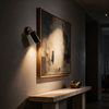 Adjustable wall spotlight angled to wash light across framed artwork in a hallway