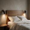 Pair of black wall spotlights flanking an oak headboard with warm bedside lighting