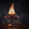 Witch hat stained glass style table lamp glowing on a dark table