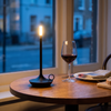 Cordless candle lamp glowing warm on a bedside table beside books