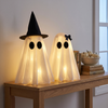 Two glowing white ghost figures with witch hat and bow on an oak hallway console