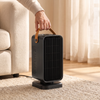 Compact ceramic space heater with leather handle lifted beside a sofa