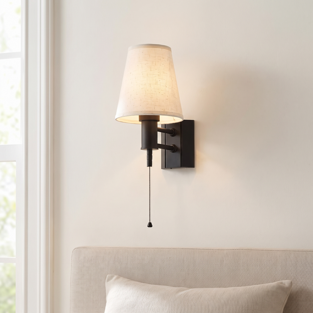 Battery wall lamp with fabric shade, black, beside a bed