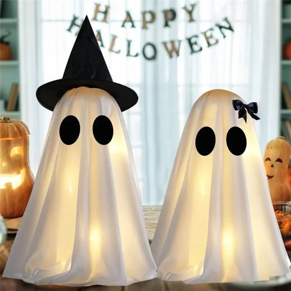 Two white ghost figures with witch hat and bow glowing on a table