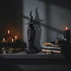 Tall black witch figurine with pointed hat on a dark shelf with candles