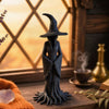 Black witch statue with bark texture on a windowsill at sunset